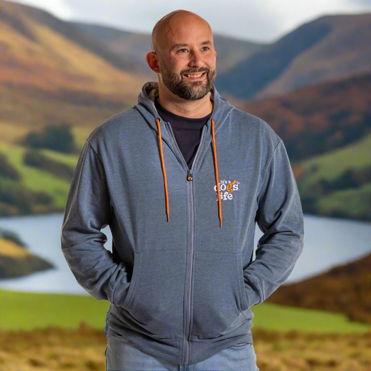 Man wearing a gray hoodie with a logo in front of a scenic background with mountains and a lake.